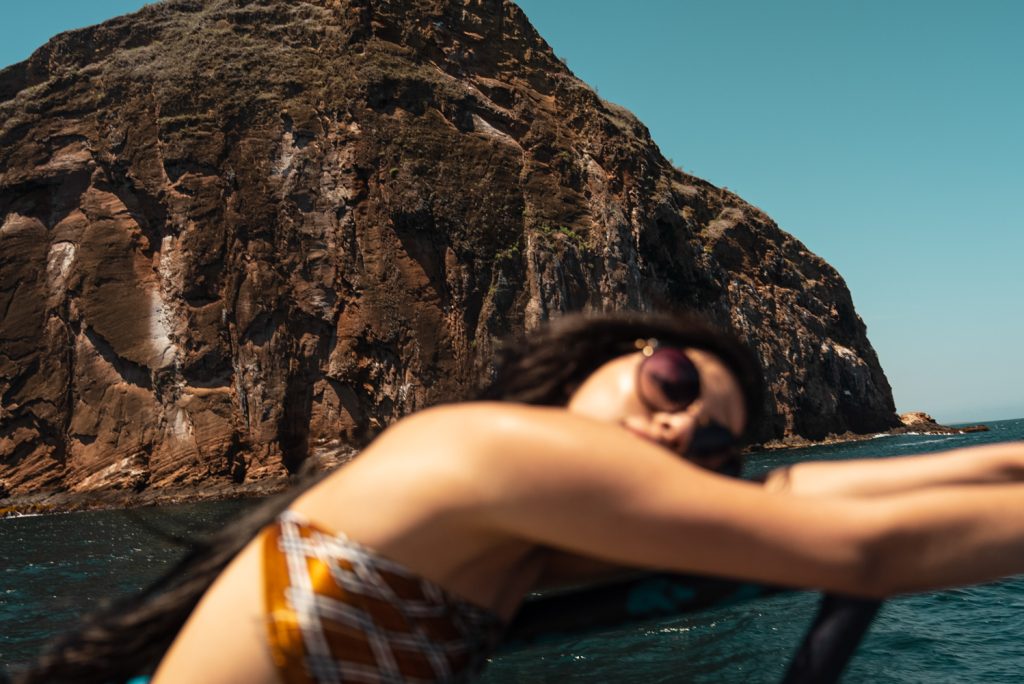 Femme en lunettes de soleil penchée sur le bord d'un bateau au pied d'une falaise en mer