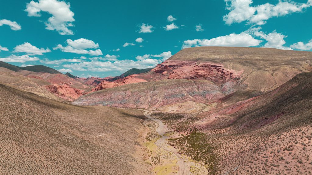 Vallée de montagnes aux roches rouges et ocre sous un ciel bleu nuageux