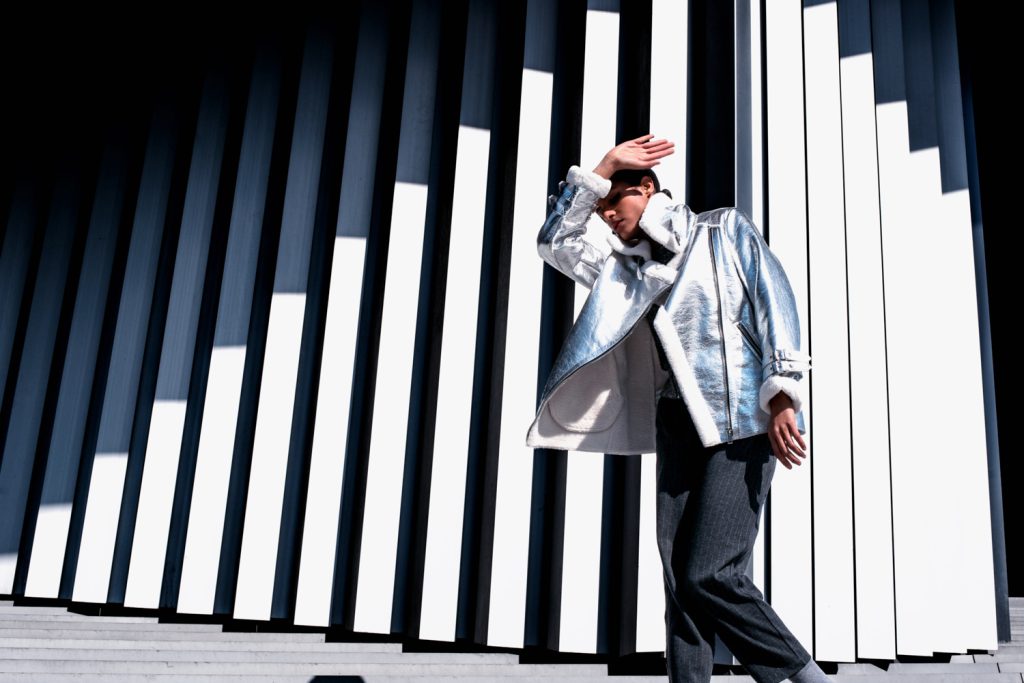 Homme en veste argentée se protégeant du soleil devant une façade à lames blanches et noires
