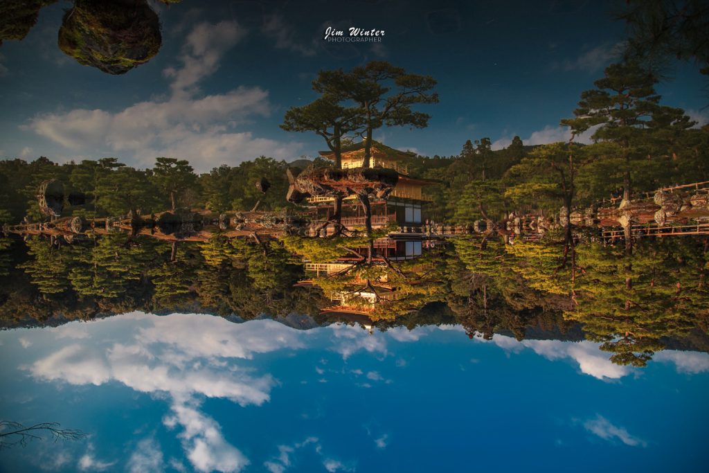 Reflet inversé d'un pavillon japonais et de pins dans un étang sous un ciel nuageux