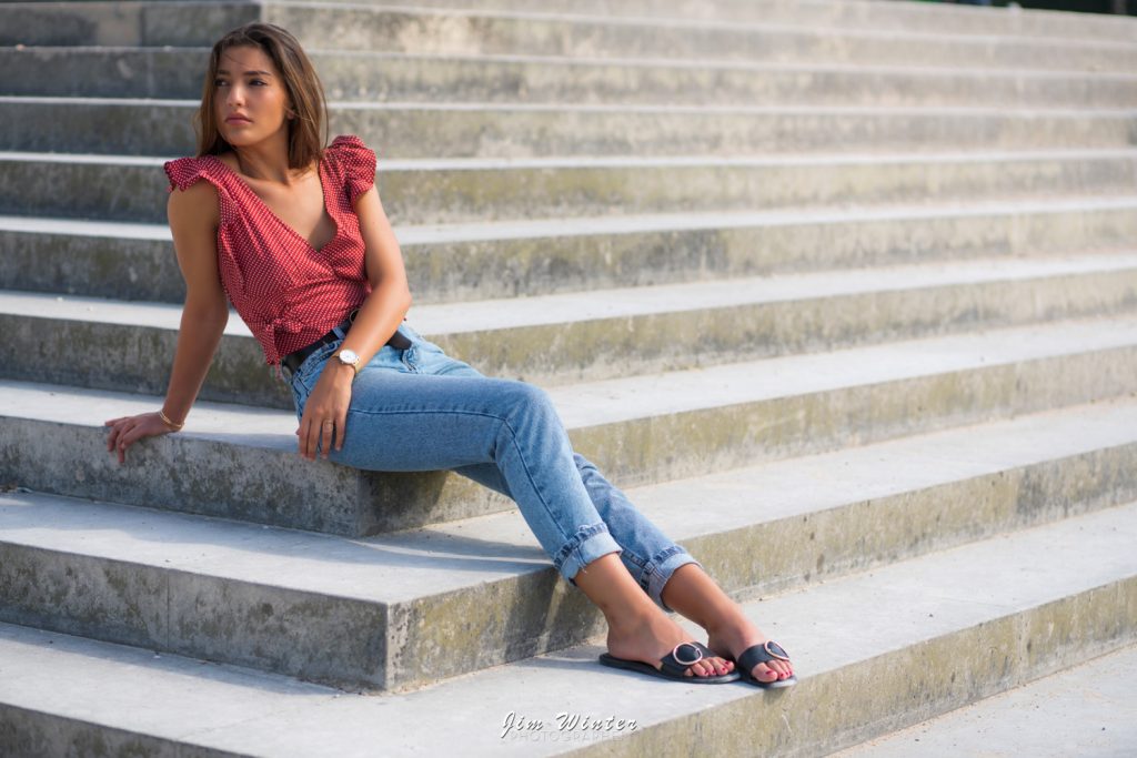 Jeune femme en top rouge et jean assise sur de grandes marches en pierre, shooting extérieur