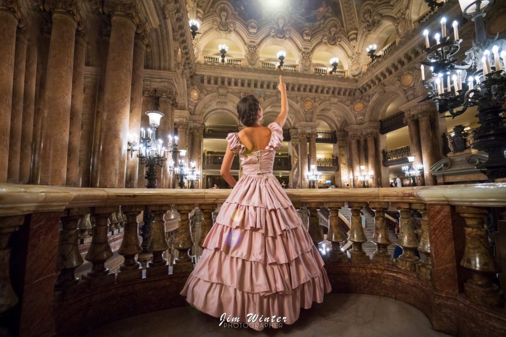 Femme en robe rose à volants au balcon du grand escalier de l'Opéra Garnier à Paris