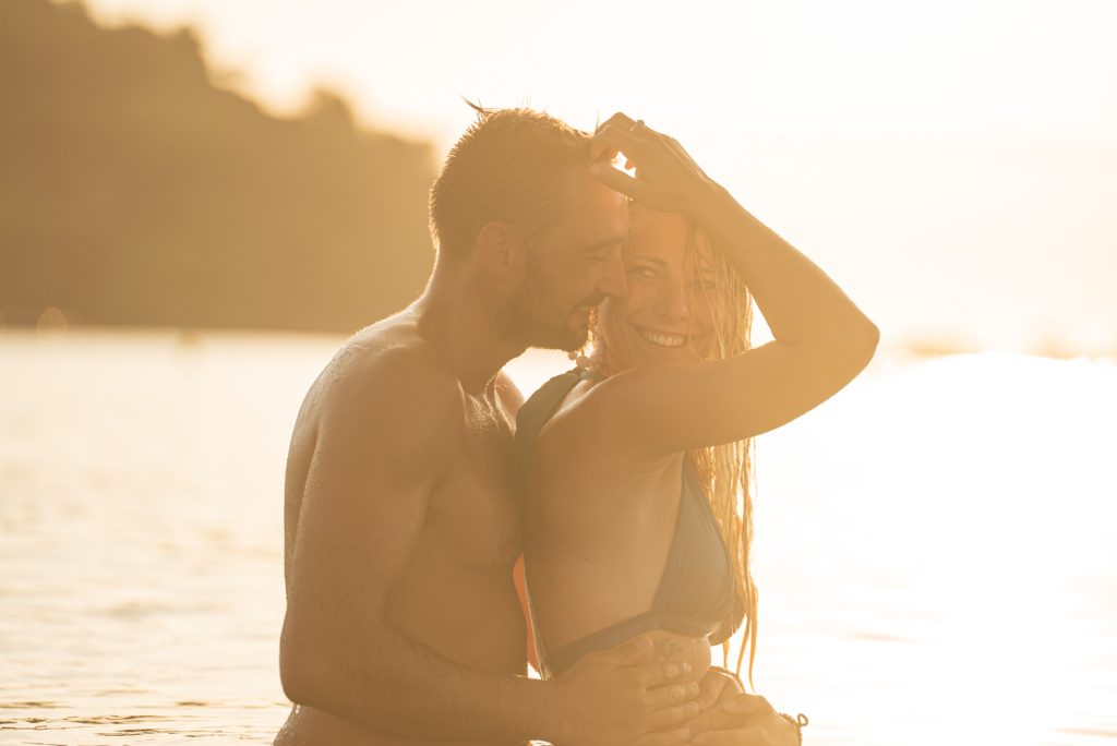 Couple enlacé et souriant dans l'eau au coucher du soleil, séance photo de couple