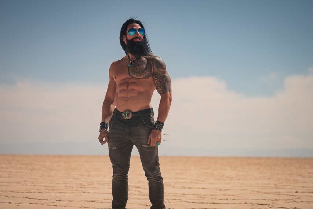 Homme barbu torse nu tatoué en lunettes de soleil debout dans un désert de sel
